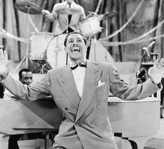 circa 1945:  EXCLUSIVE Full-length image of American jazz singer and bandleader Cab Calloway  (1907 - 1994) crouching with his hands in the air while performing in front of a pianist and a drummer on a stage.  (Photo by Metronome/Getty Images)